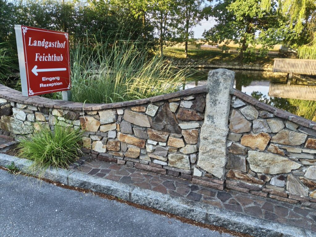 geschwungene Sichtmauerwerk-Abgrenzungsmauer rund um einen Teich